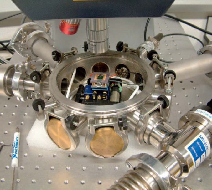Photograph of the environmental chamber, showing a sample attached to the vacuum-compatible XY stages. The long-focal length lens can be seen above the sample, which is attached to the Polytec Micro Systems Analyzer Differential Vibrometer.