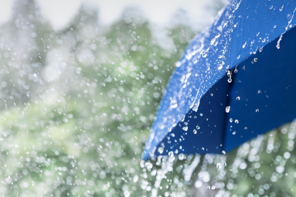 Blue umbrella under heavy rain against nature background. Rainy weather concept.
