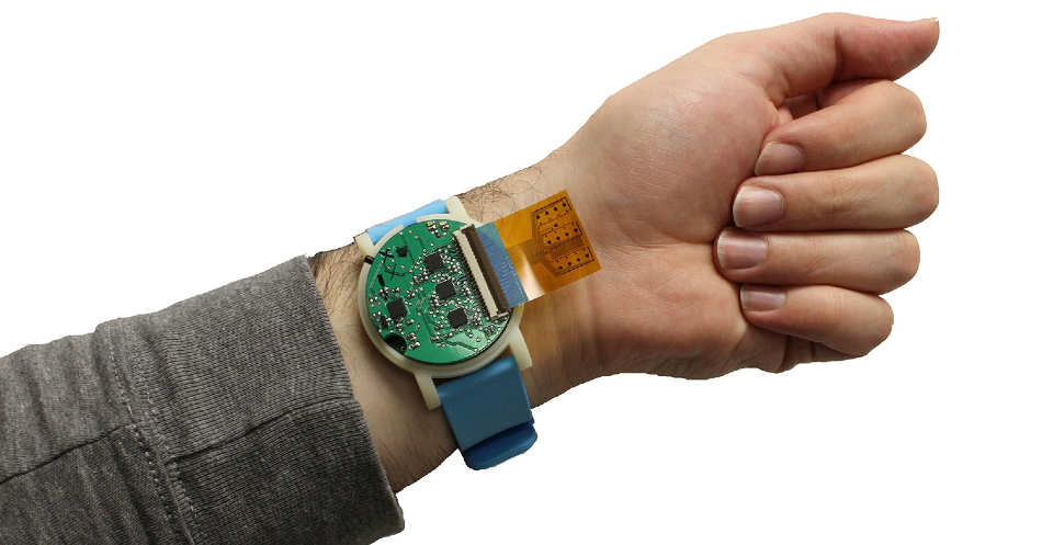 The metabolite monitoring device, shown here, is the size of a wristwatch. The sensor strip, which sticks out in this photo, can be tucked back, lying between the device and the user’s skin